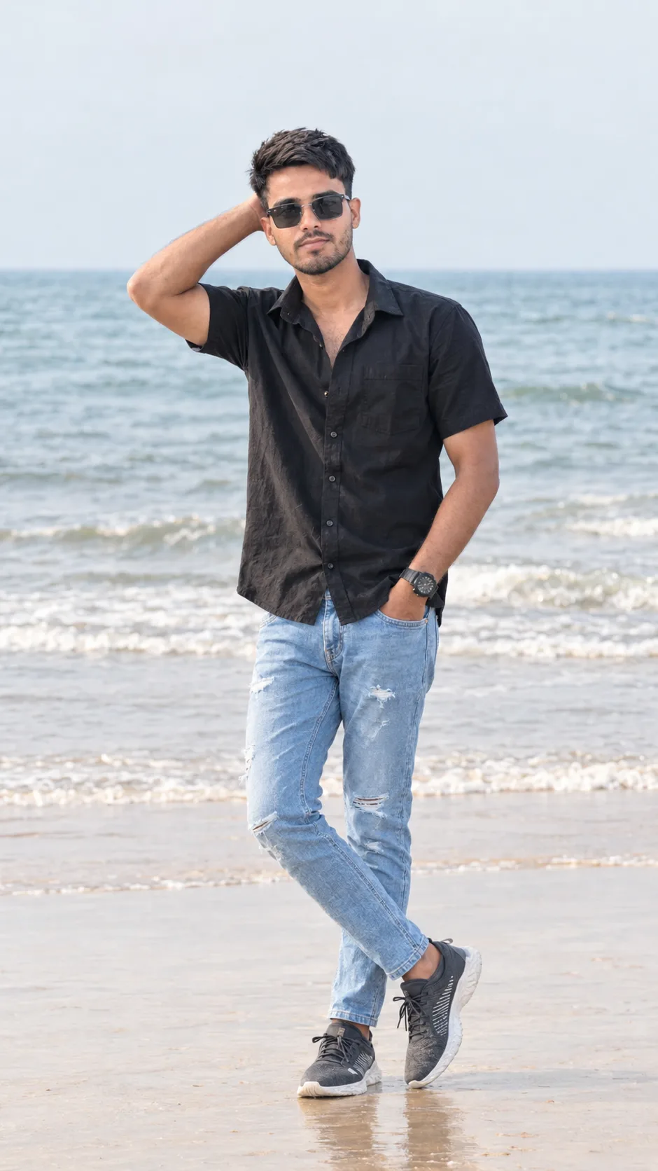 Create a highly realistic full-body fashion portrait of a stylish young South Asian/Indian man standing casually on a beautiful beach with