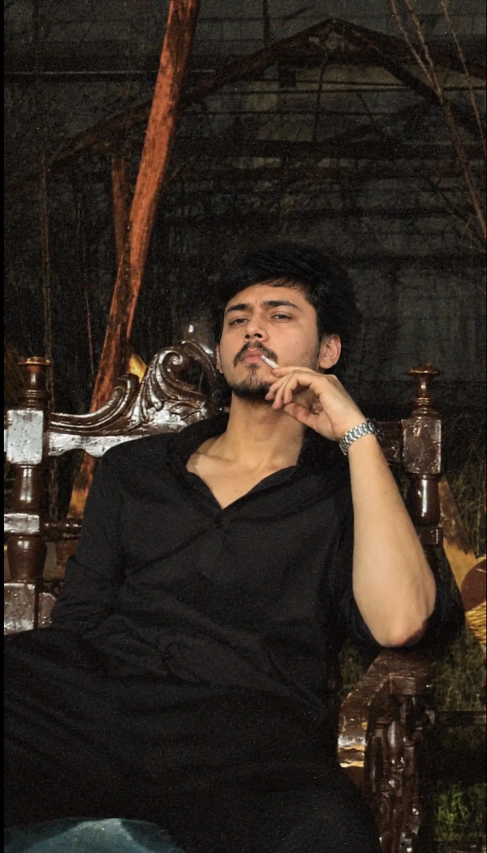 Create a highly realistic cinematic portrait of a young South Asian man sitting confidently on an ornate antique wooden chair in a dark