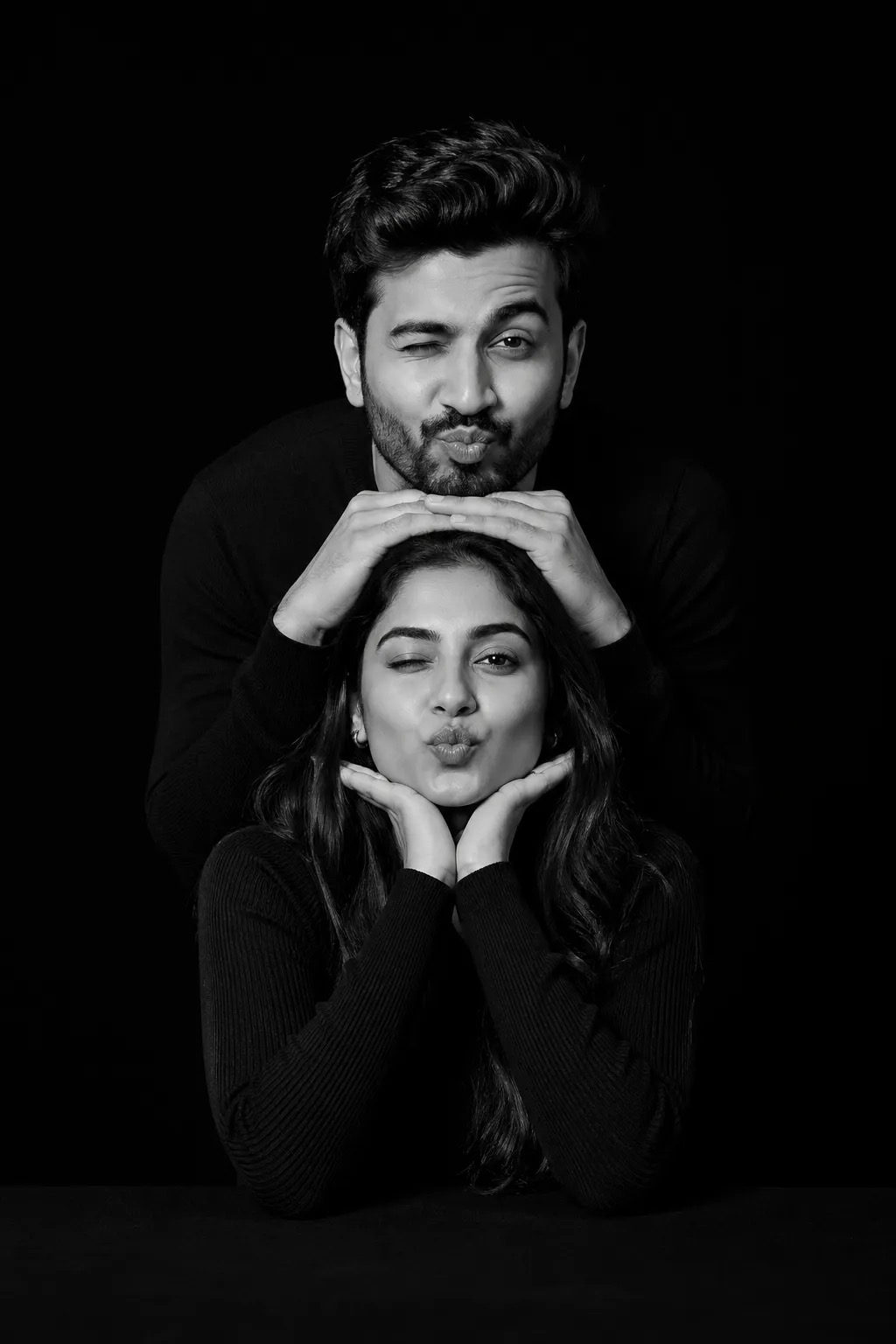 Edit the image A dramatic black-and-white studio portrait of a playful couple of two stacked vertically in a creative pose.