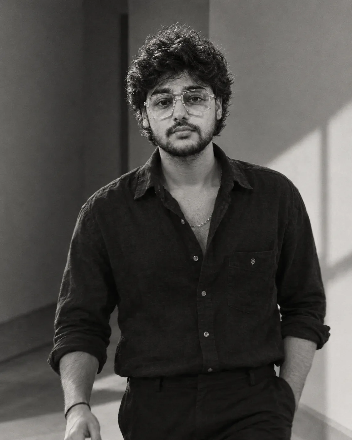 "A moody black-and-white portrait of a young man with short, soft, tousled dark curly hair falling loosely over his forehead, looking