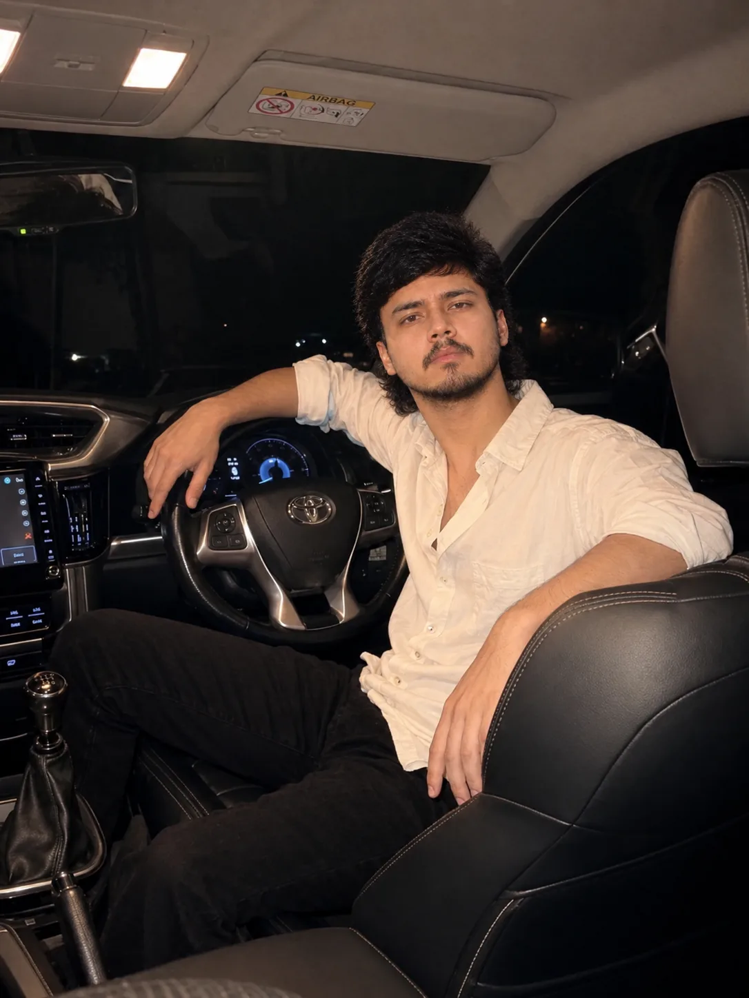 Ultra-realistic cinematic night-time portrait of a young Indian man sitting confidently in the driver’s seat of a modern Toyota car,