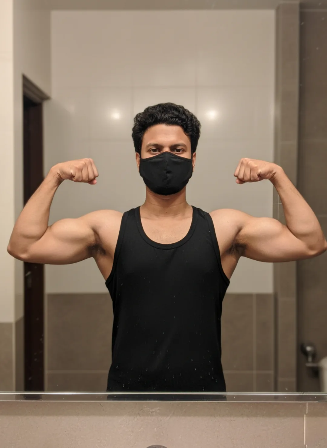 A high-resolution mirror selfie of an athletic young South Asian man posing inside a modern indoor setting, captured with a clean