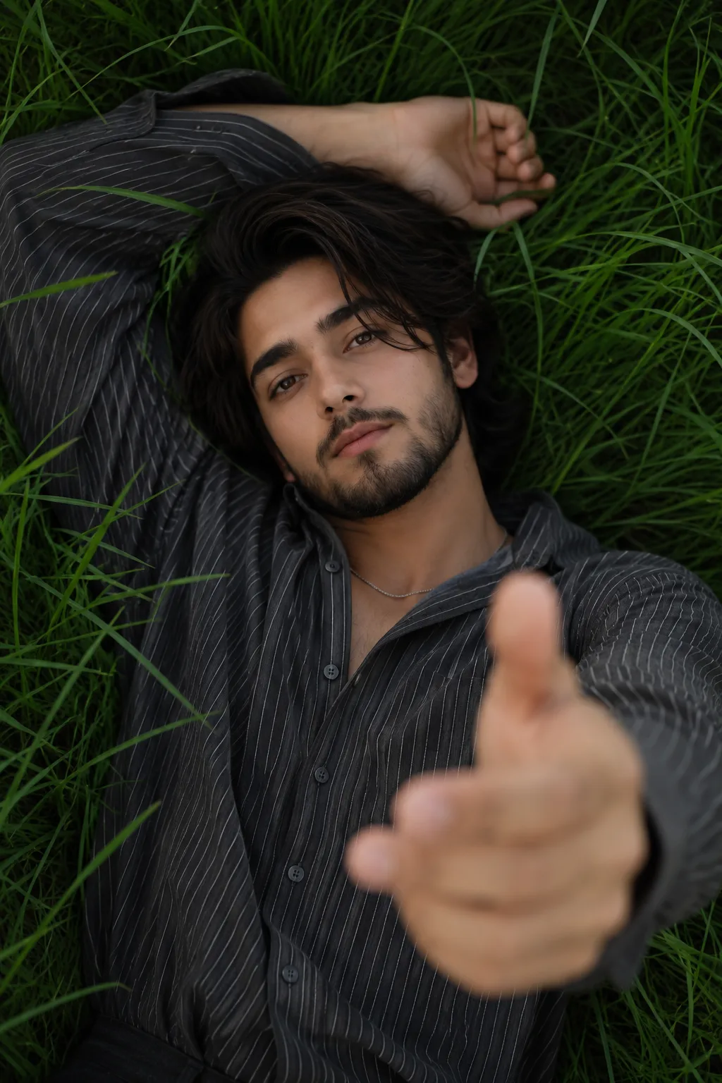 Close-up top-down view of a handsome young man lying flat on his back in vibrant green grass.
