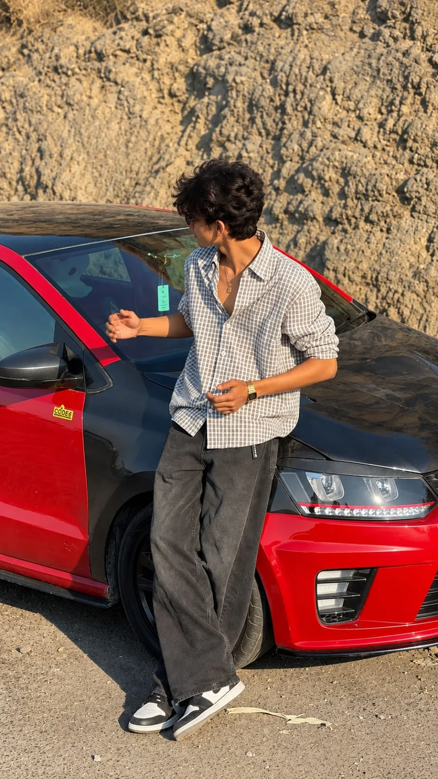 Ultra-realistic full-body fashion photograph of a young man standing casually beside a sporty red-and-black luxury car, parked outdoors