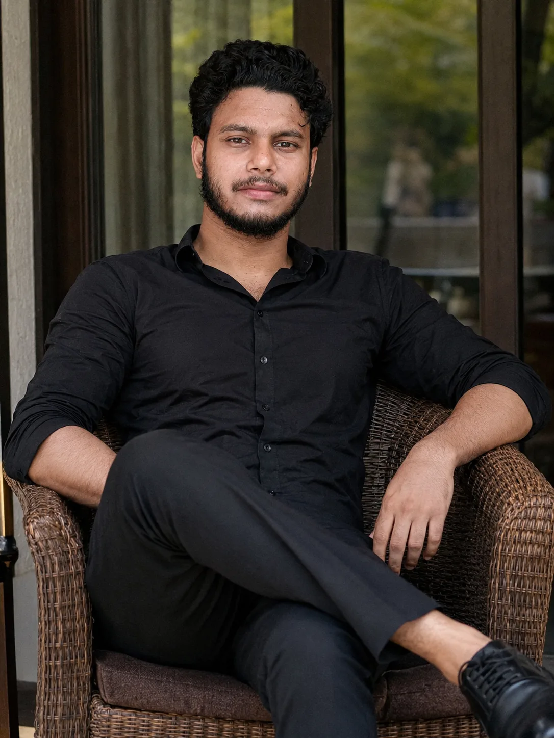 A professional high-resolution photographic portrait of a 26-year-old south Asian man with curly black hair, a neatly trimmed beard, and