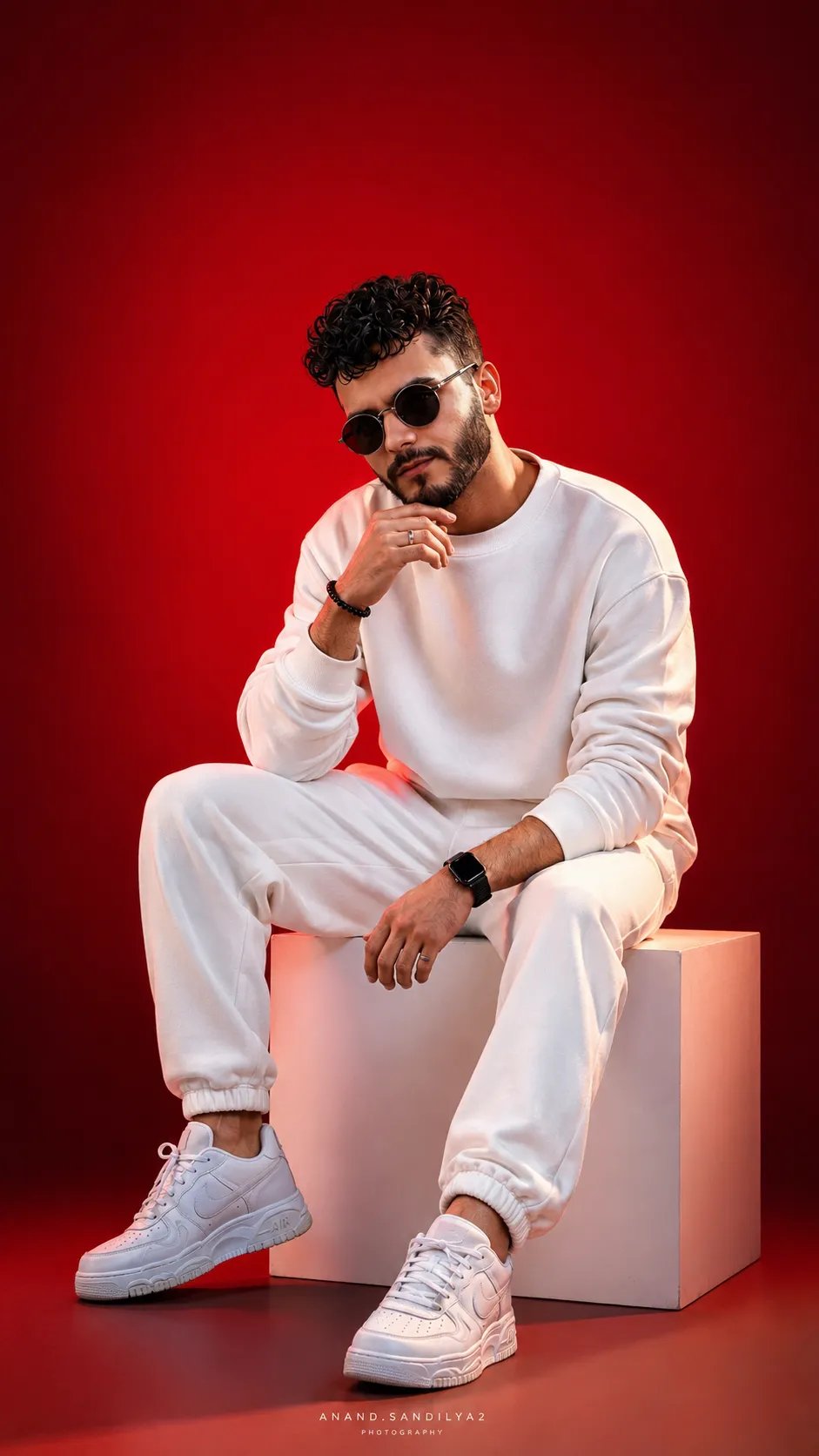 Create a striking studio portrait of a man sitting on a white cube against a bold red gradient background.