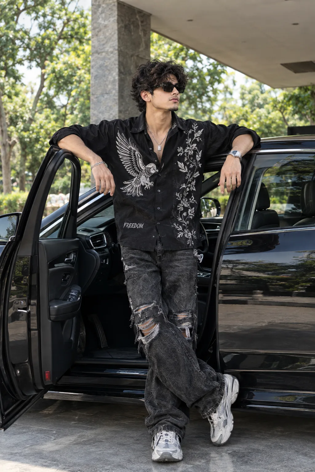 Stylish Young Man in Embroidered Black Shirt Leaning on Open Door of Luxury Car
