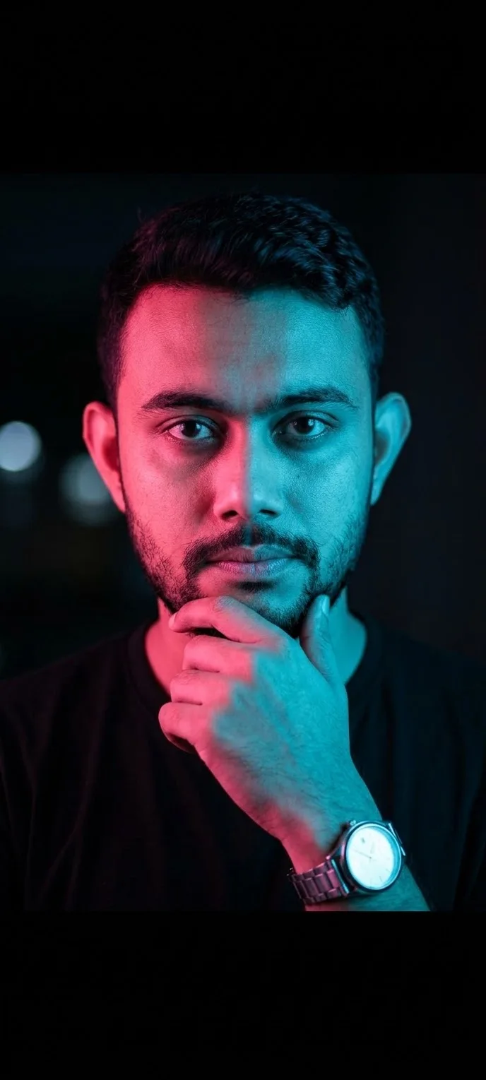 A man with a beard and short dark hair is captured in a striking portrait, illuminated by dramatic dual-colored lighting.