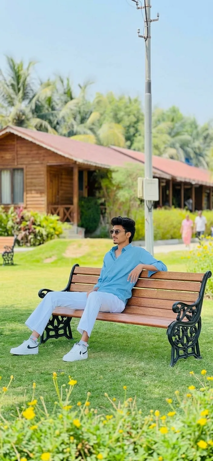 A photorealistic vertical full-length shot capturing the young South Asian man from the reference image seated outdoors on a polished