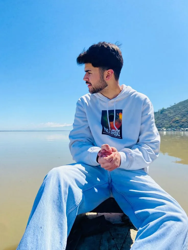 A photorealistic vertical medium shot of the young South Asian man from the reference image, faithfully preserving his exact recognizable