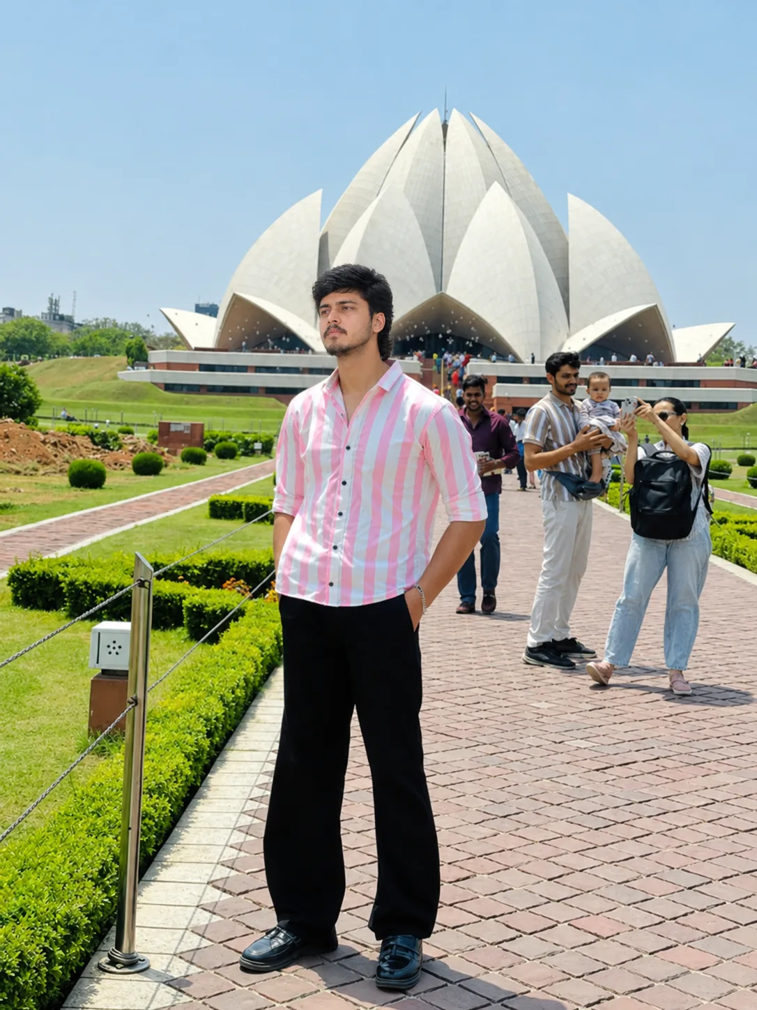 A realistic high-resolution full-body travel photograph of a young South Asian man standing confidently on a paved pathway in front of the