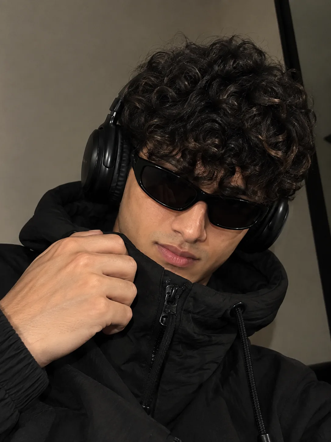 Photorealistic close-up portrait of a young man wearing a black puffer jacket, black over-ear headphones, and sleek black wraparound