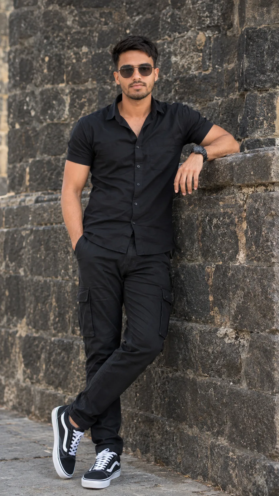 Create a photorealistic full-body fashion portrait of a stylish young South Asian man standing casually against an old rugged dark-gray