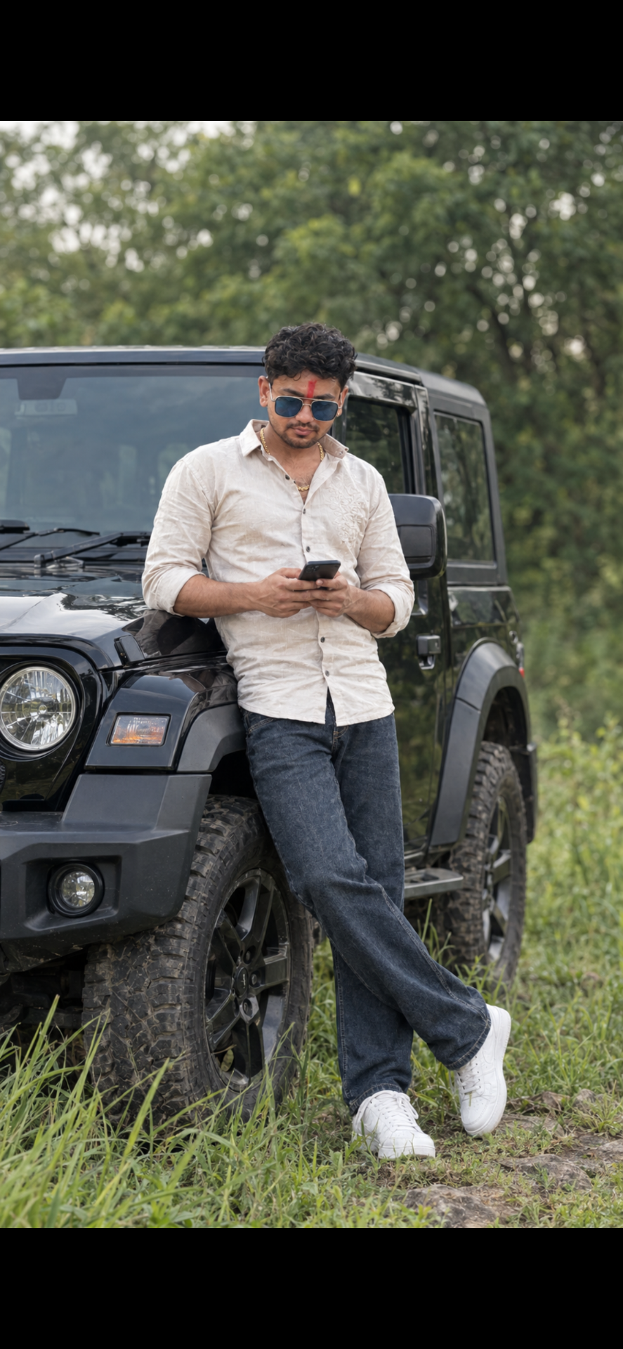 A cinematic outdoor portrait of a stylish young South Asian man with wavy dark hair and a short beard, wearing dark sunglasses, a