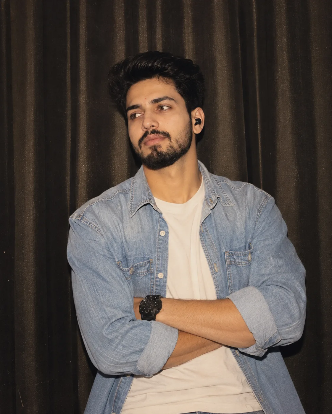 Ultra-realistic portrait of a young South Asian man with messy black hair and light beard, wearing a light blue denim shirt over a white