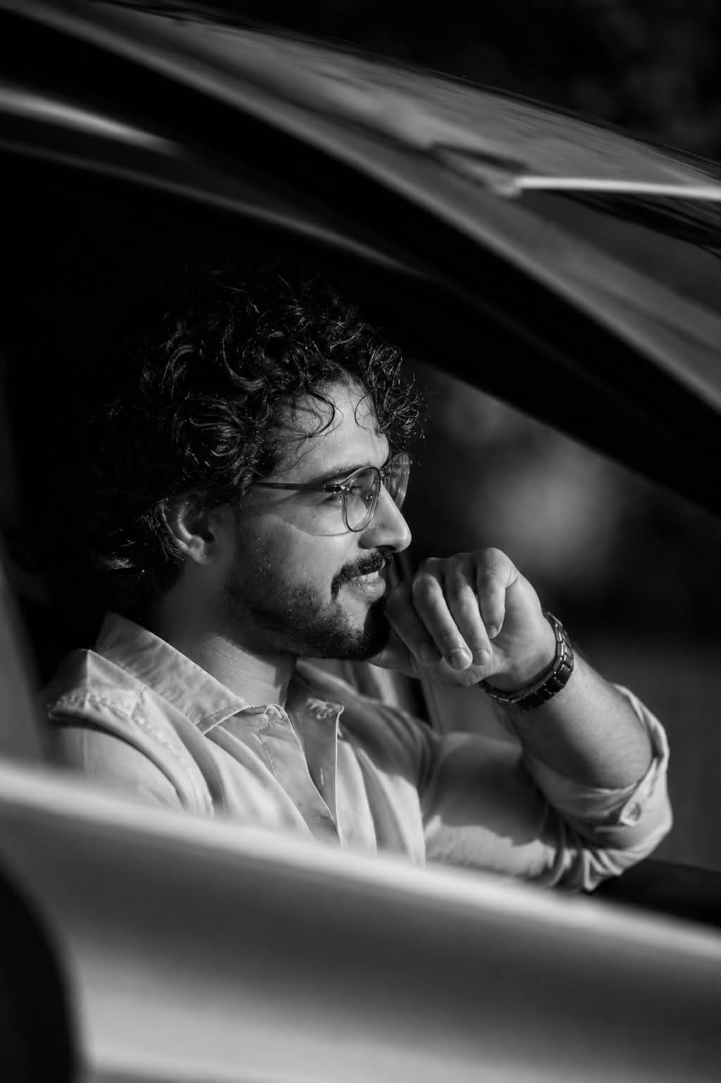 Cinematic high-contrast B&W editorial portrait: Subject in side profile inside a car, looking thoughtfully out the side window, hand near
