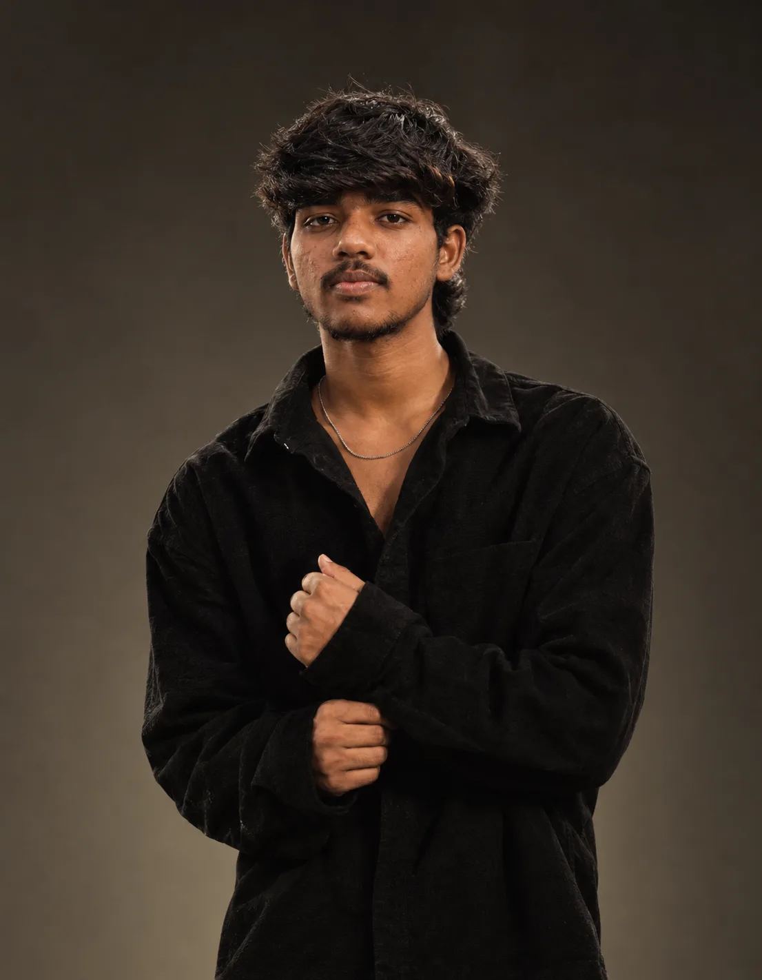 Ultra-realistic cinematic fashion portrait of a stylish young South Asian man standing against a simple dark warm-gray studio background.
