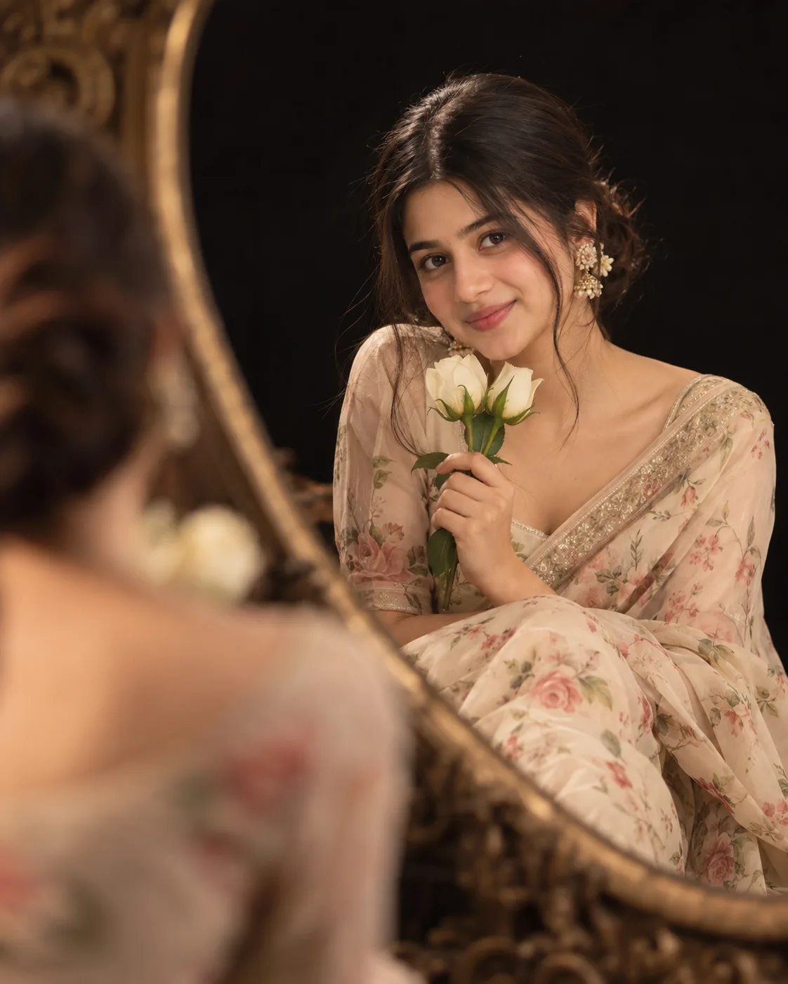 Ultra-realistic cinematic portrait of a young Indian woman in a soft beige/cream floral saree, sitting gracefully and looking directly at