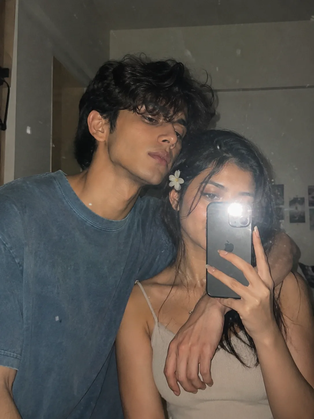 Create an ultra-realistic candid iPhone mirror selfie of a young adult man and young adult woman standing very close together indoors,