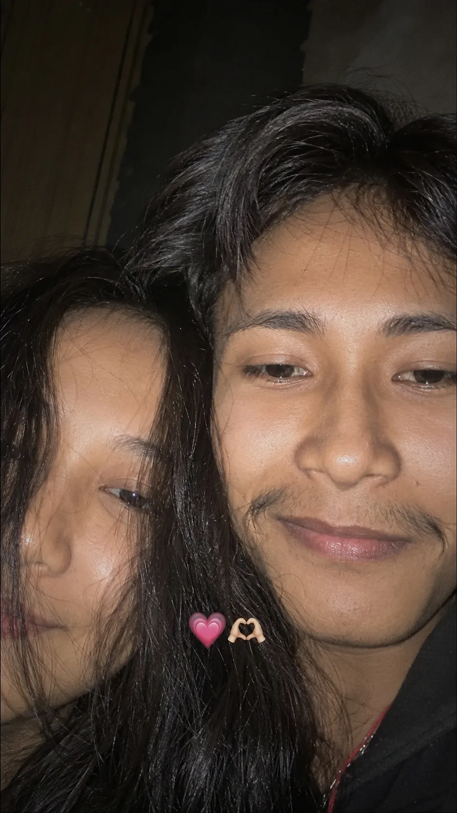 Create a highly realistic, natural close-up smartphone selfie of a young Indian couple sitting very close together indoors at night.