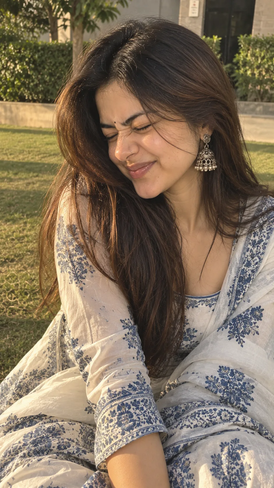 Prompt: A warm, candid close-up portrait of a young South Asian woman sitting outdoors on a lawn, making a playful, cute grimacing face