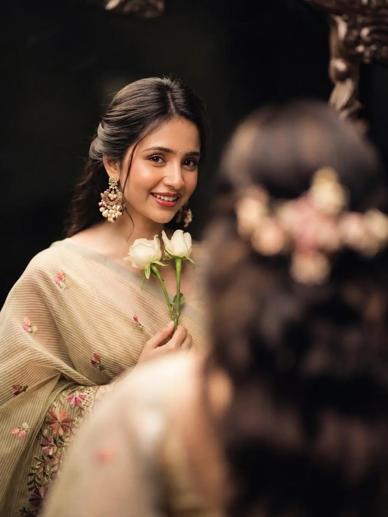 Ultra-realistic cinematic portrait of a young Indian woman in a soft beige/cream floral saree, sitting gracefully and looking directly at