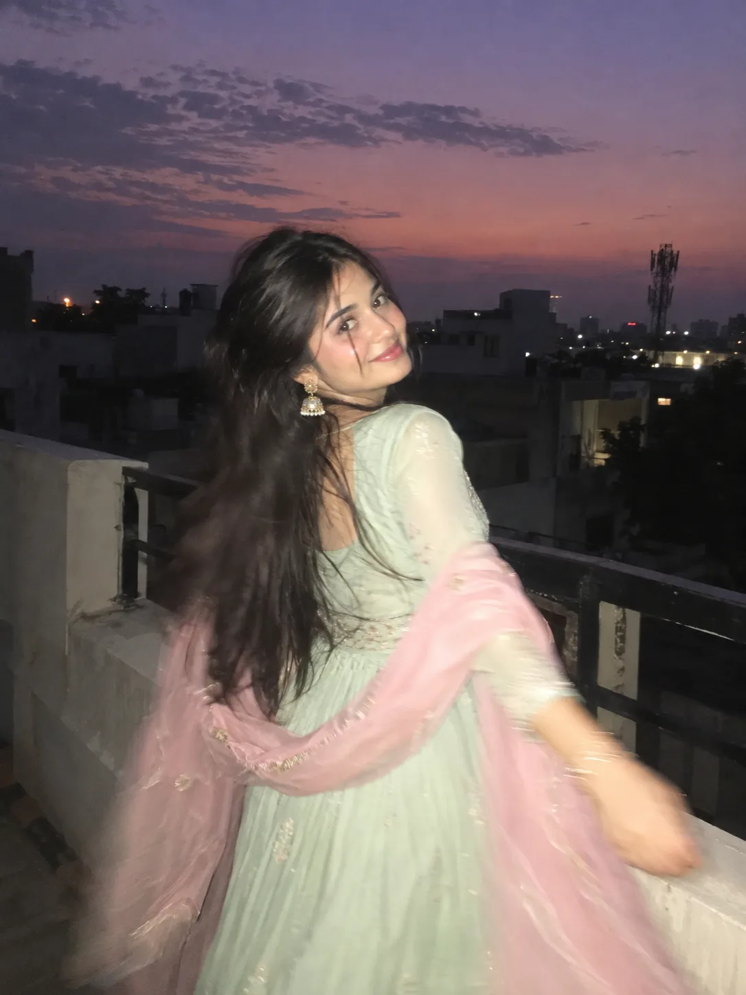 Create an ultra-realistic candid rooftop portrait of a woman (the reference Image given) during blue hour, just after sunset, with a dusky