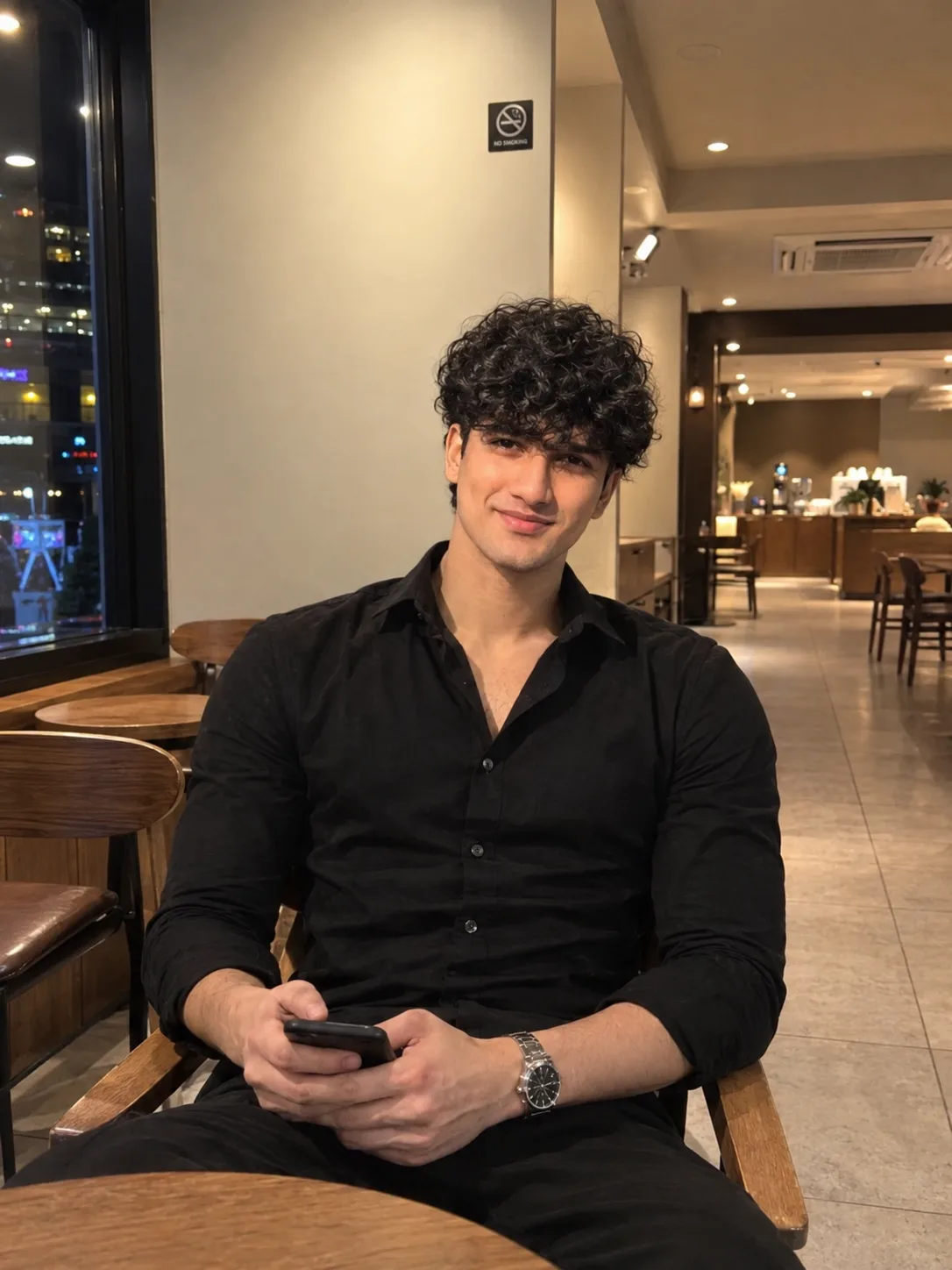 Ultra-realistic high-resolution portrait of a young man sitting casually inside a modern café at night.