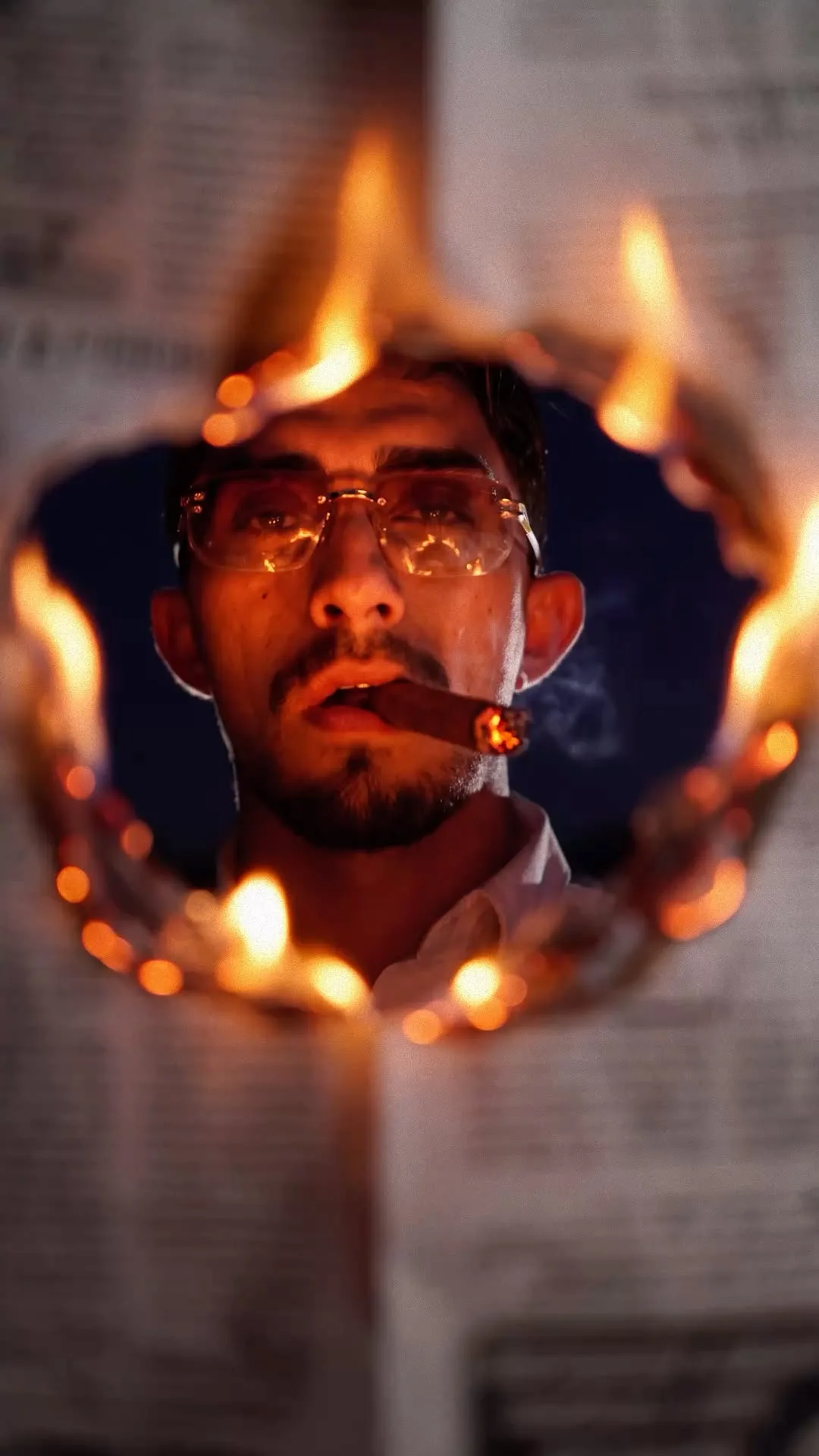 "A dramatic cinematic close-up portrait of a fierce young man with a sharp beard and clear-framed eyeglasses, holding a lit cigar between