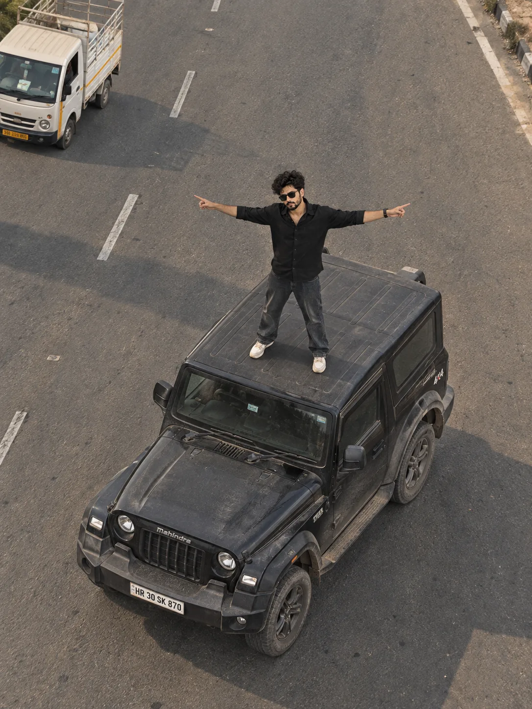 High-angle drone shot, aerial view of a young Indian man with stylish black hair and a light beard, standing on the roof of a matte dark