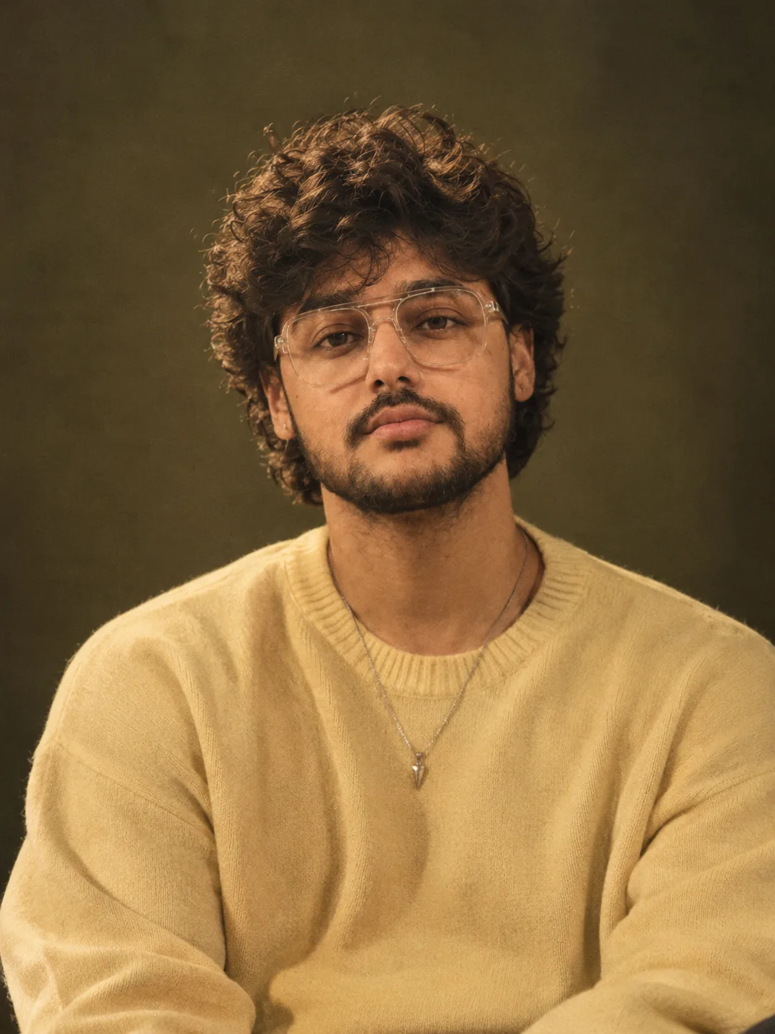"A moody, cinematic studio portrait of a young man with thick, messy, tousled black wavy hair falling in a loose fringe over his forehead,