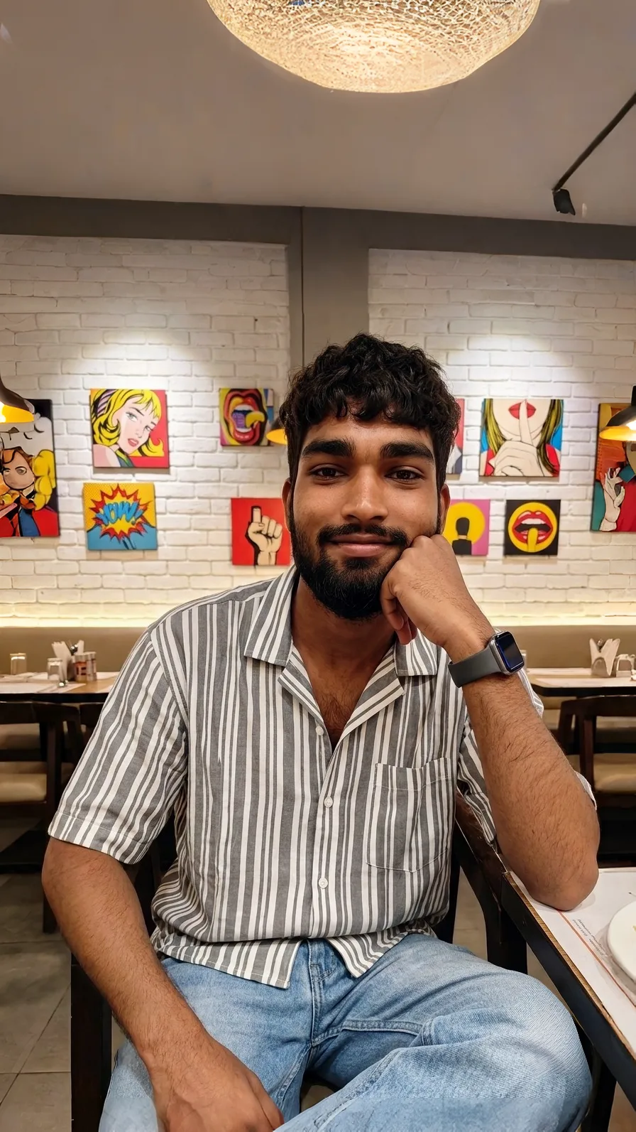 A photorealistic vertical medium shot of the young South Asian man from the reference image, faithfully preserving his recognizable facial