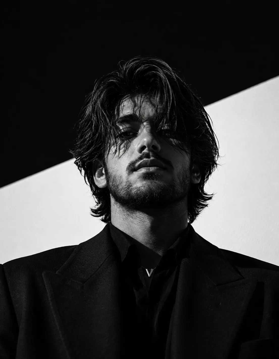 A highly cinematic, photorealistic black-and-white editorial portrait of a handsome young adult man photographed from a dramatic low angle,