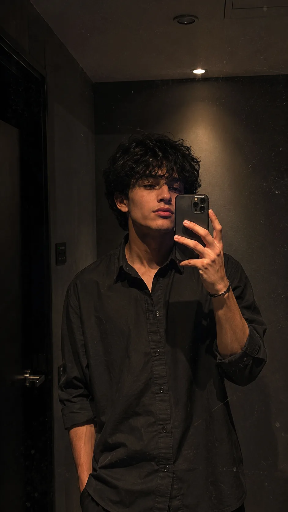 Visual Style: Ultra-realistic smartphone mirror selfie × dark minimalist interior × contemporary menswear × intimate candid photography ×