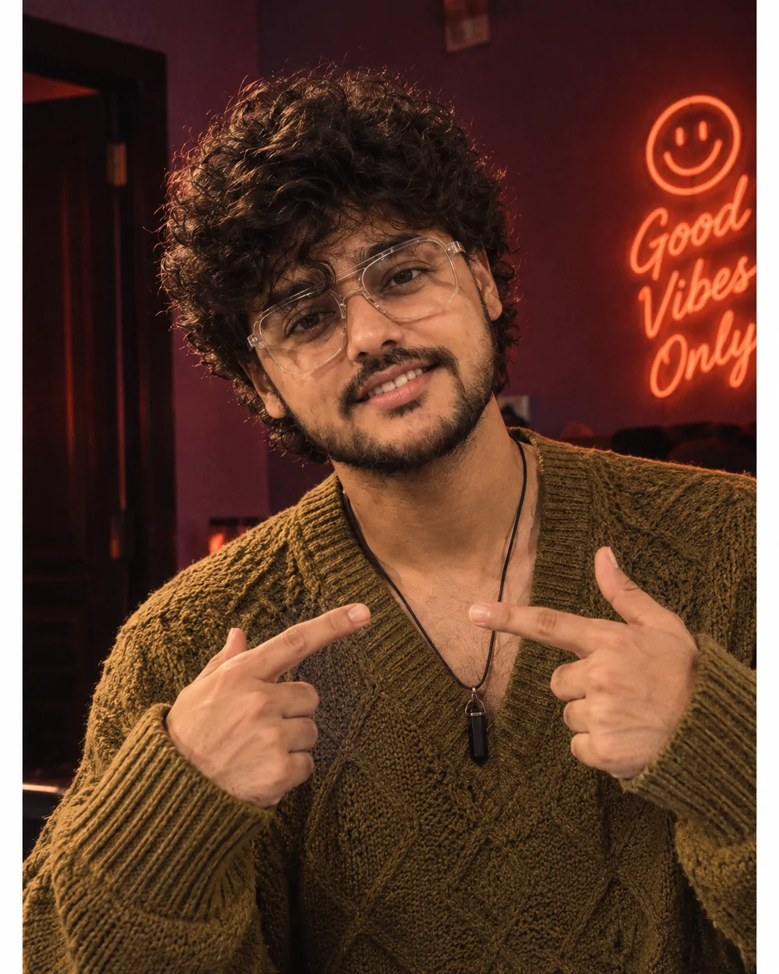 "A playful, close-up portrait of a young man with thick, voluminous dark curly hair styled in a tousled fringe that falls over his forehead