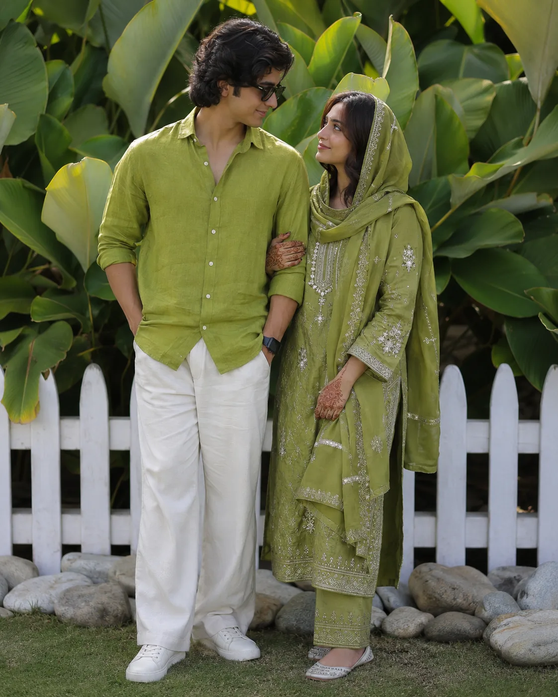 A full-length, eye-level cinematic photograph of a young South Asian couple standing together outdoors, sharing an intimate look.