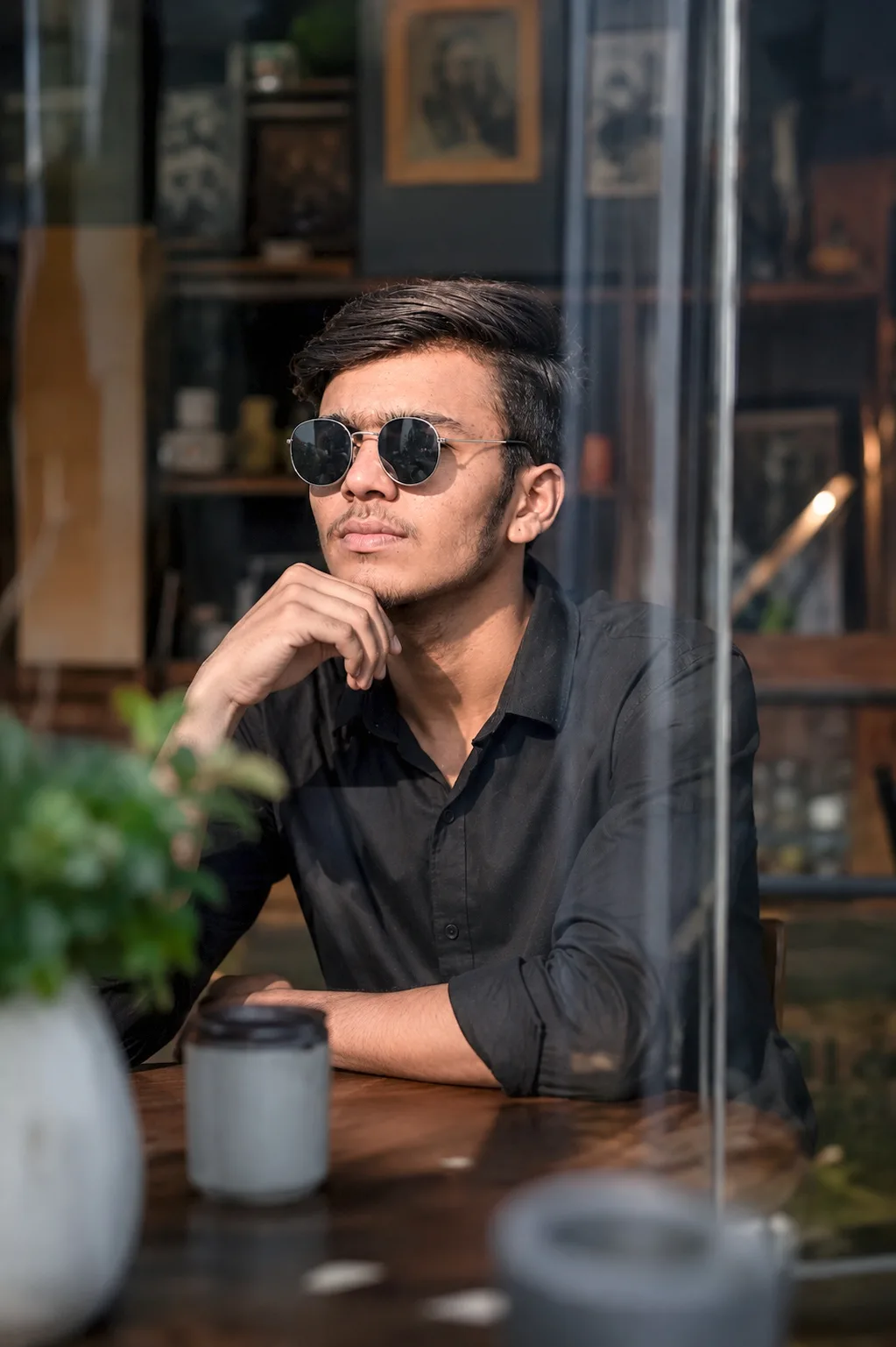 Create an ultra-realistic high-resolution DSLR portrait photograph of a young man sitting casually at a stylish café table, photographed