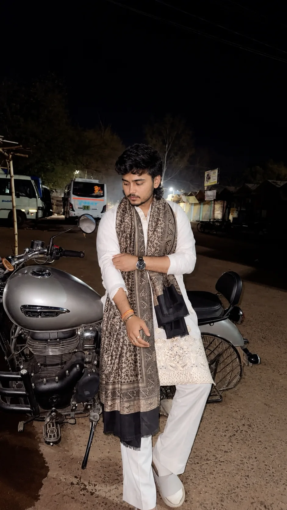 Create an ultra-photorealistic full-body nighttime portrait of the same young South Asian man from the reference image, standing casually