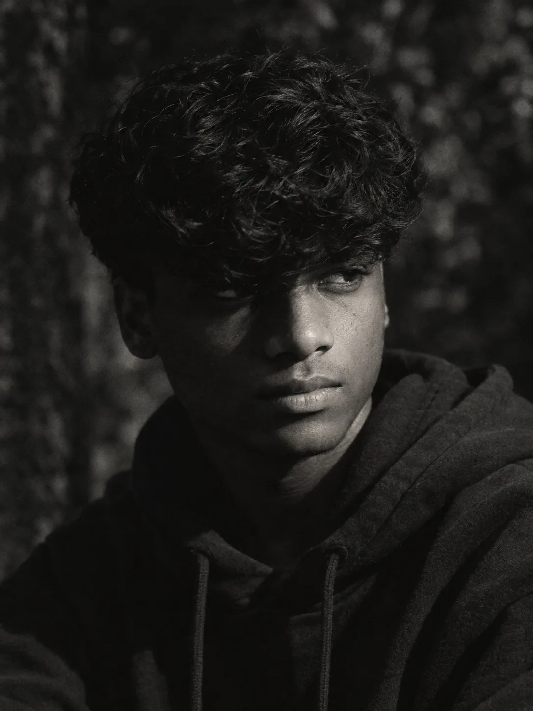 A dramatic cinematic close-up portrait of a young man with wavy dark hair, captured in moody black and white.