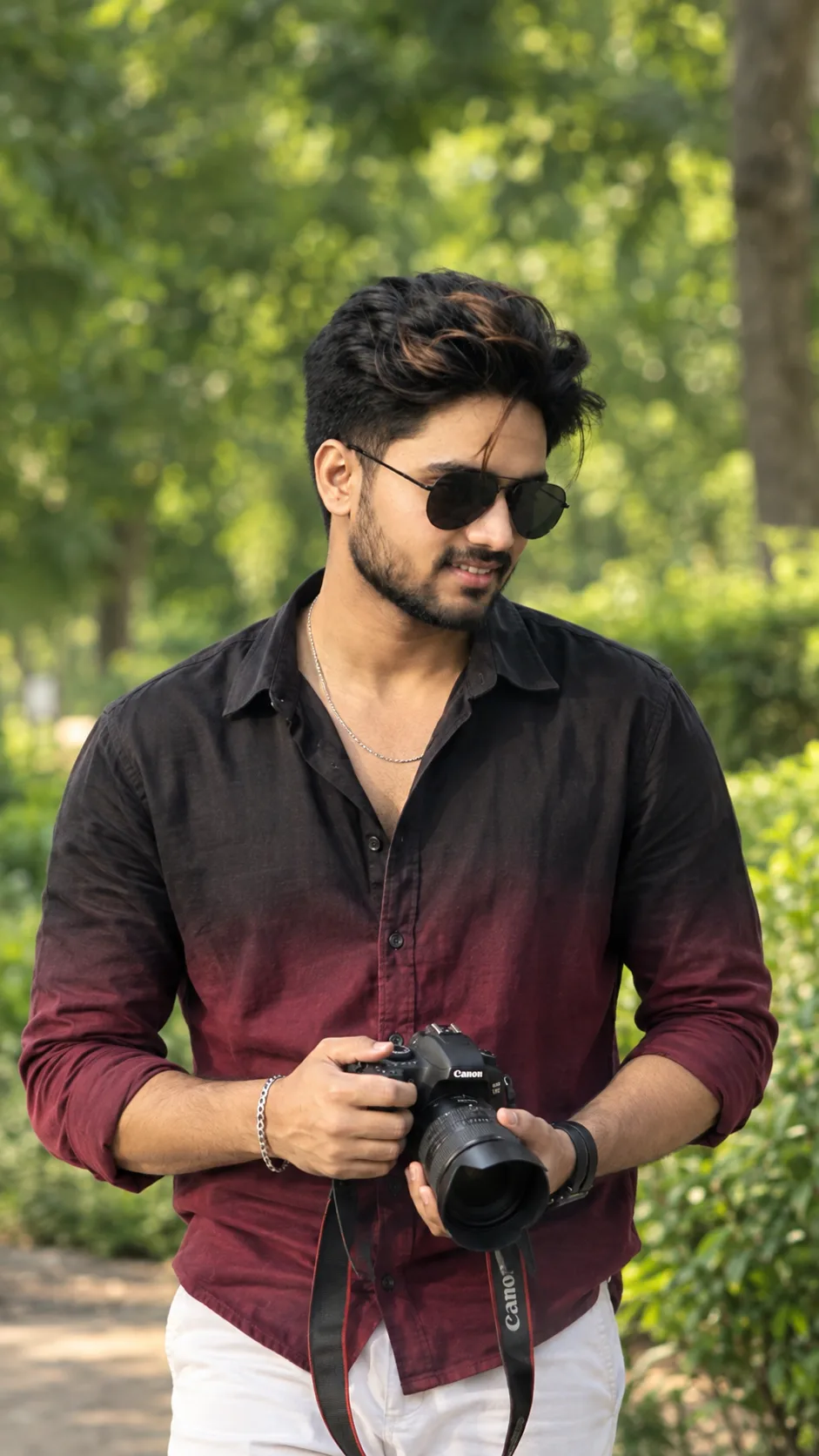 A sharp, candid 9:16 portrait of a handsome young South Asian man standing outdoors in a lush green park.
