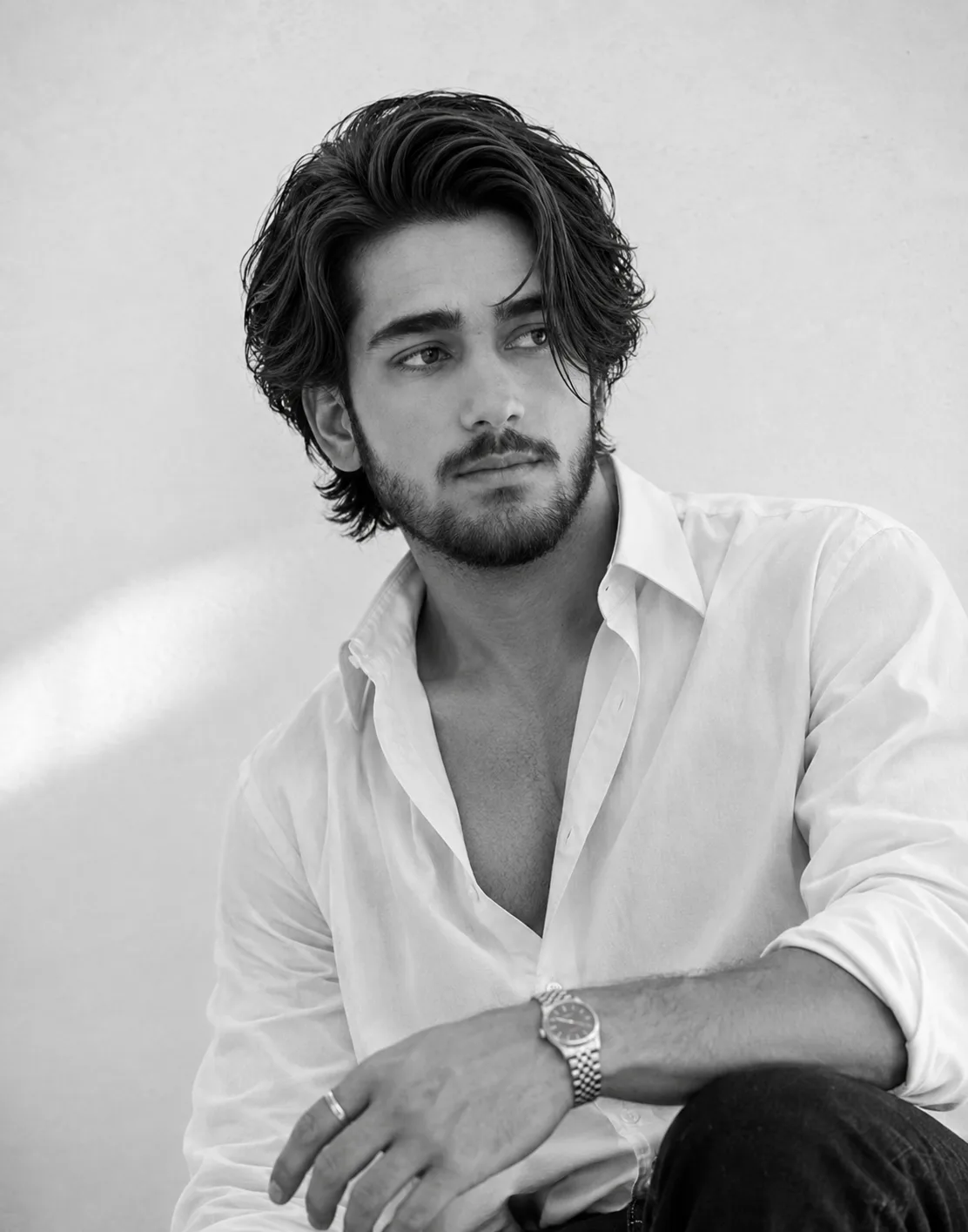 A highly photorealistic vintage black-and-white editorial portrait of a handsome young adult man with thick, naturally wavy dark hair,