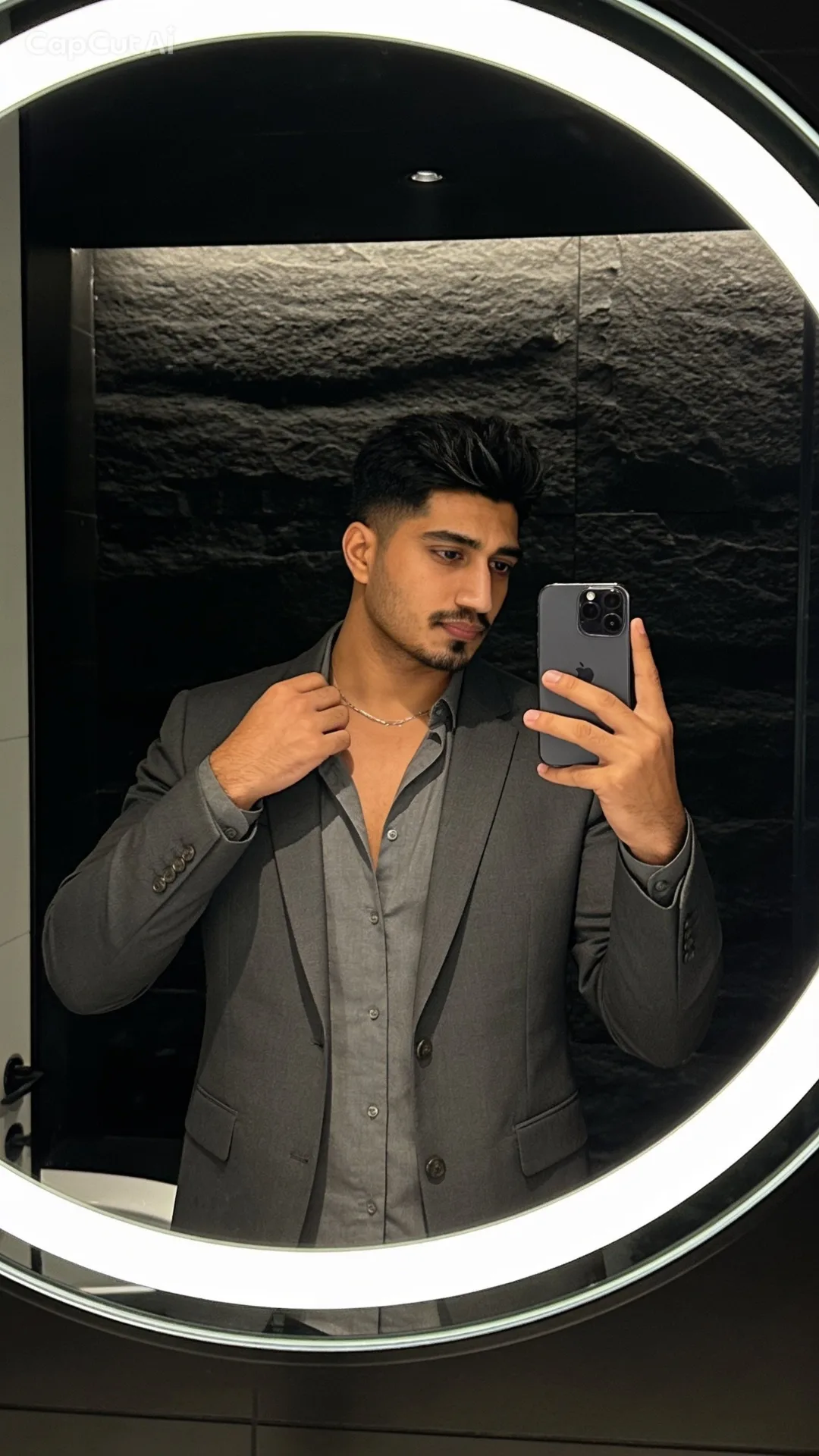 A realistic mirror selfie portrait in a modern, dimly lit room with a textured black stone wall.