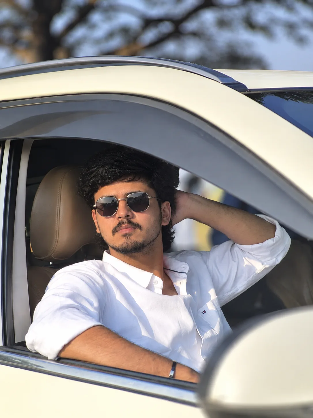 Create an ultra-realistic, photorealistic vertical portrait of a young South Asian/Indian man sitting casually in the driver’s seat of a