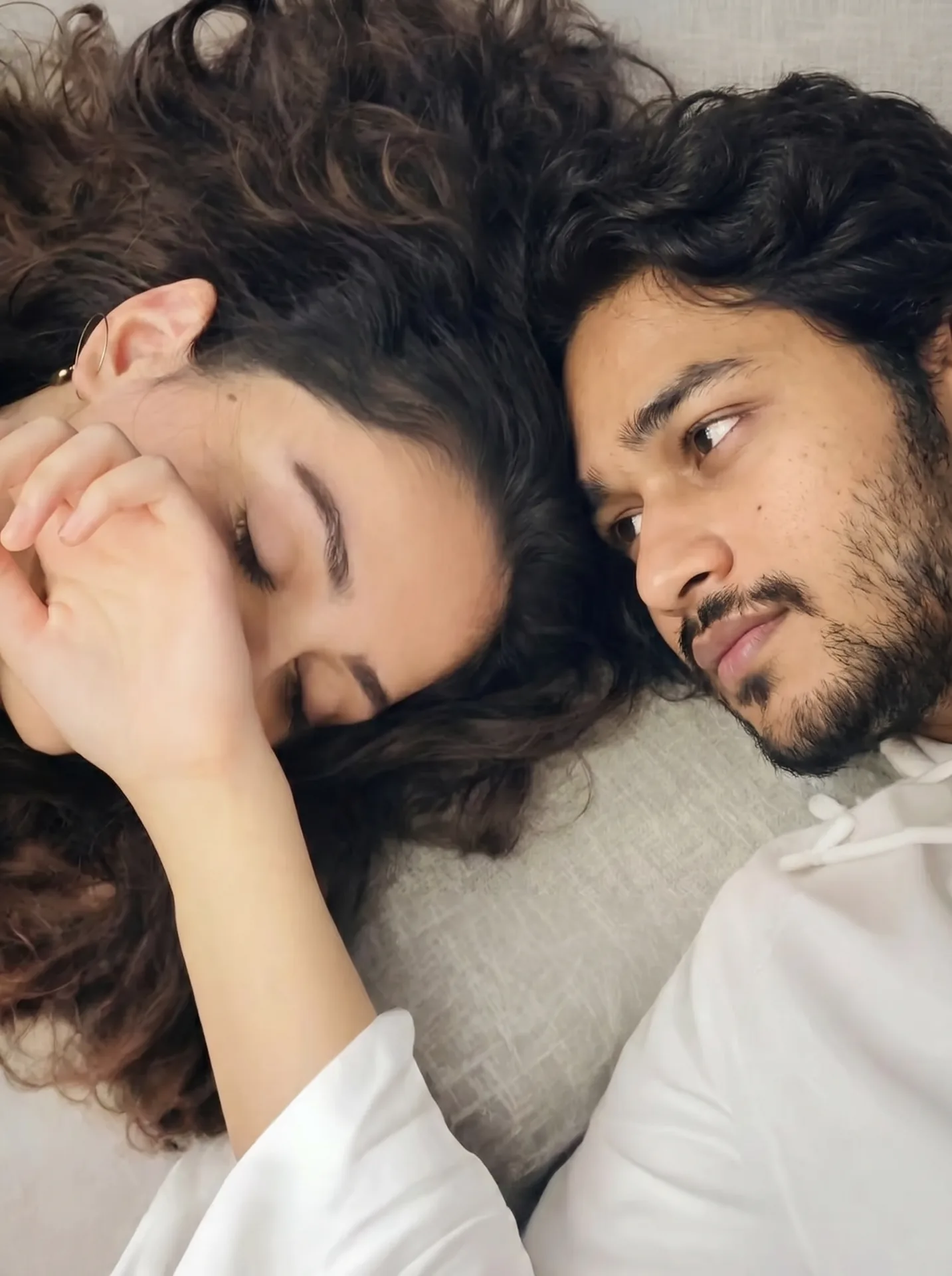 **Prompt:** Close-up top-down portrait of a young couple lying side by side on a soft light gray textured fabric, heads touching.