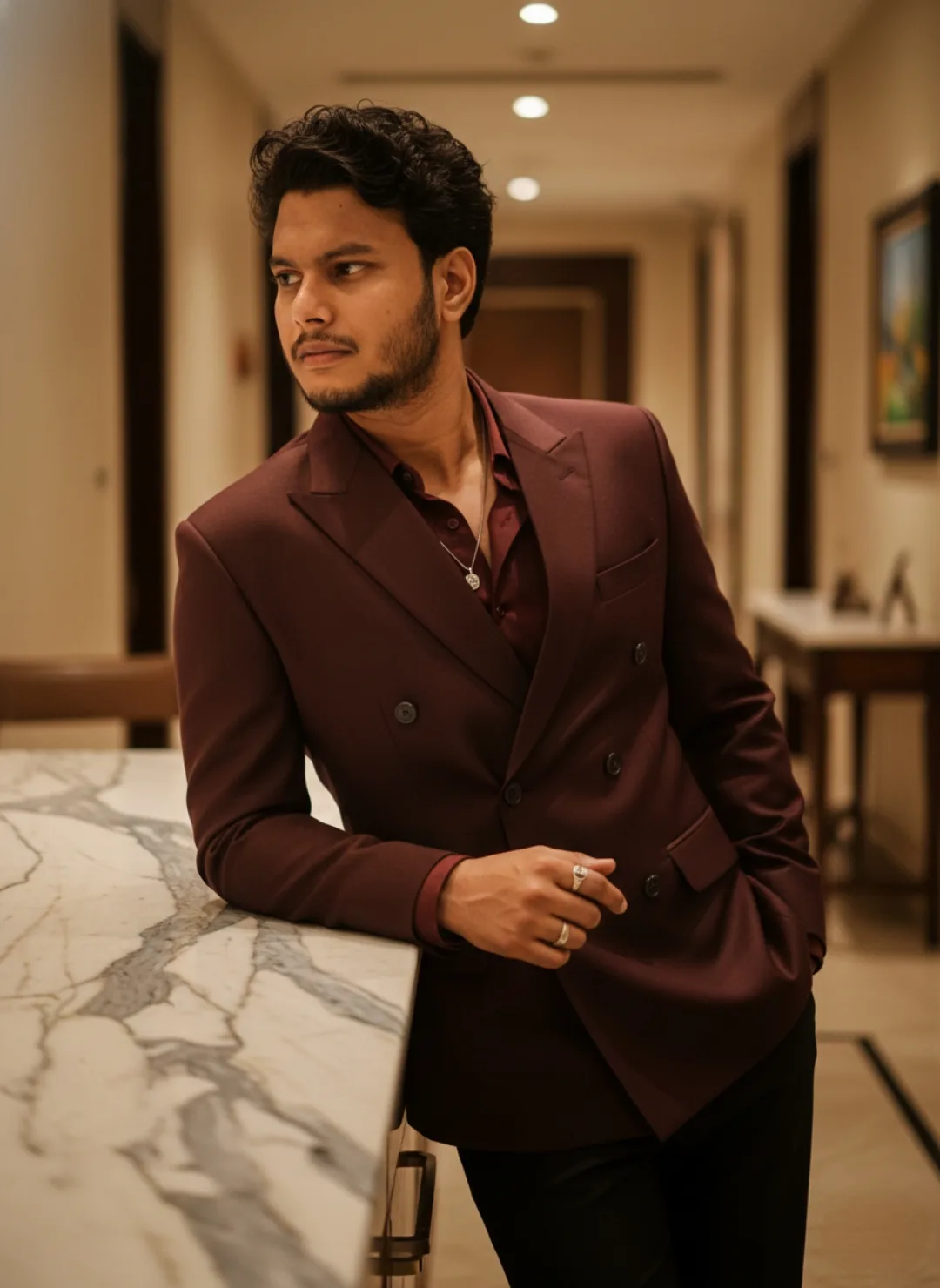 A photorealistic medium shot of a young Indian man in his early 20s standing in a luxurious modern hotel hallway.