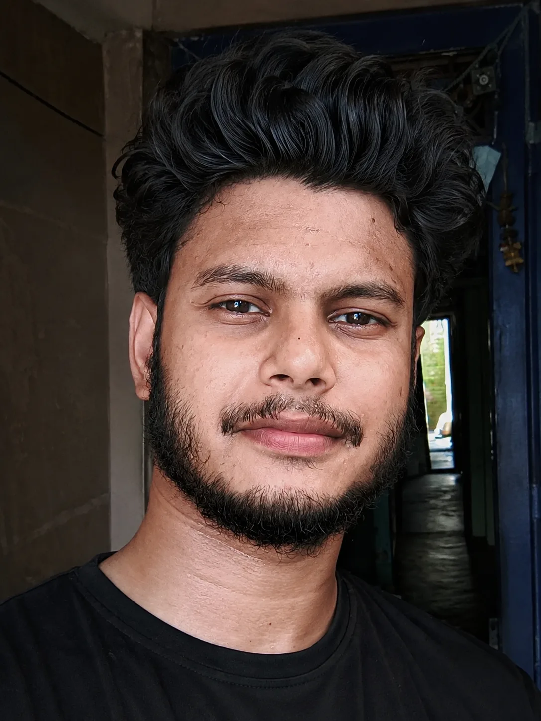 A realistic close-up selfie portrait of a young South Asian man in his early 20s, with medium-brown skin tone that has a slight natural