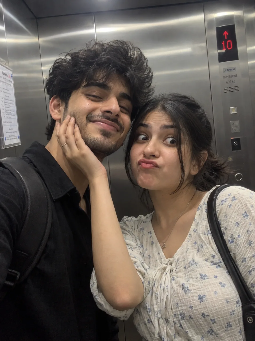 A realistic, candid mirror selfie or cl ose-up shot of a young South Asian couple inside an elevator.