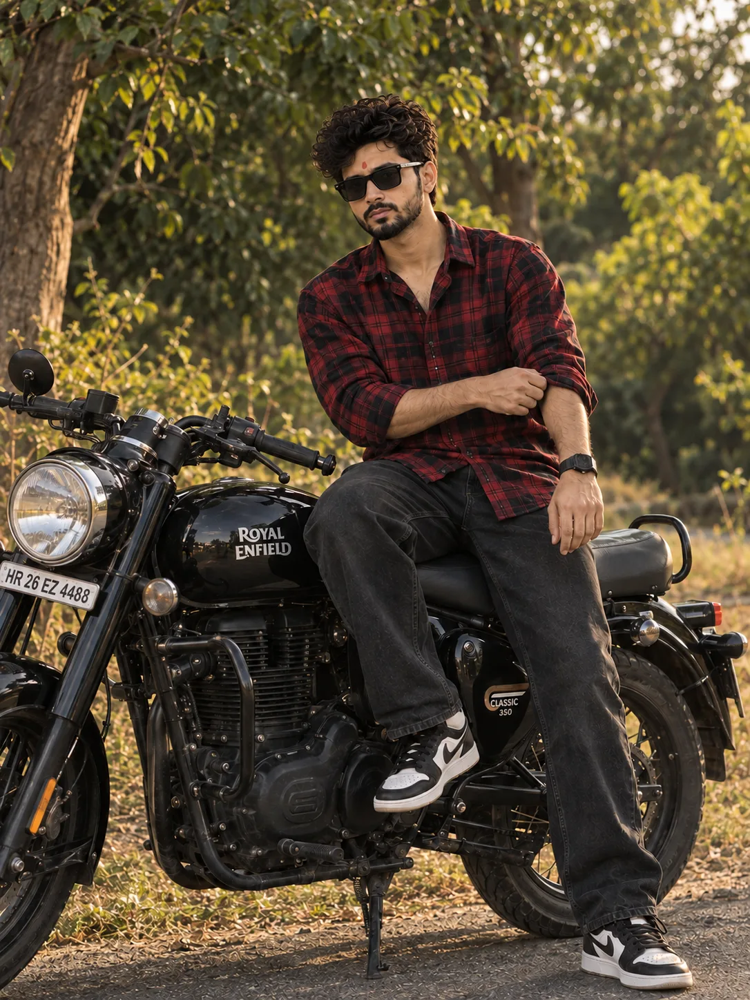 A stylish young man sitting on a classic black motorcycle outdoors during late afternoon.