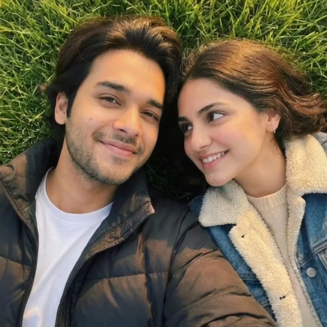 Detailed Image Generation Prompt > A top-down overhead photo of a young South Asian couple lying side-by-side on green grass.