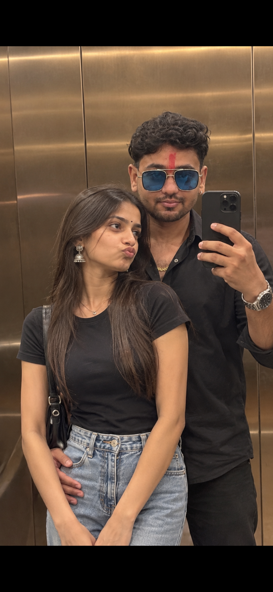 A photorealistic vertical medium shot capturing a candid mirror selfie of the young South Asian couple inside an elevator, faithfully